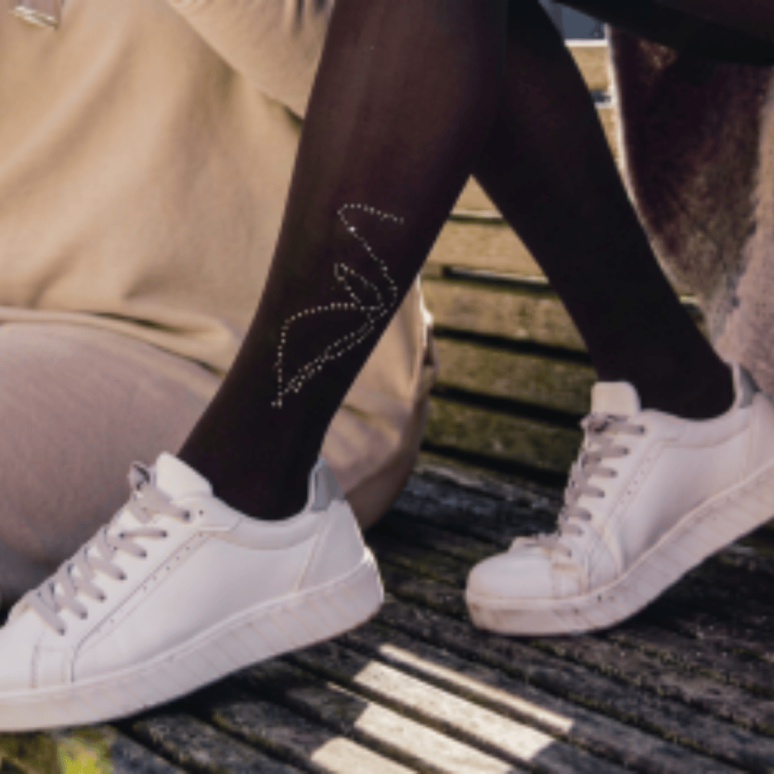 Black tights with a sparkling rhinestone design on one leg, paired with white sneakers, shown on a person sitting on a wooden bench.